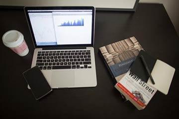 Alt text: Laptop, coffee cup, open books, and papers on a dark desk.