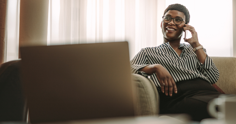 Woman sitting on bed with laptop on her lap and cell phone against her ear