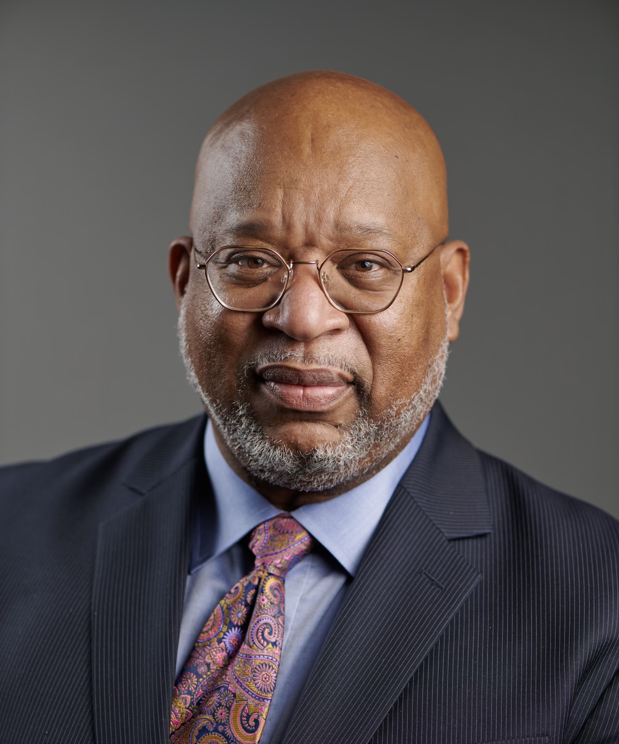 A person wearing glasses, a suit, and a patterned tie.