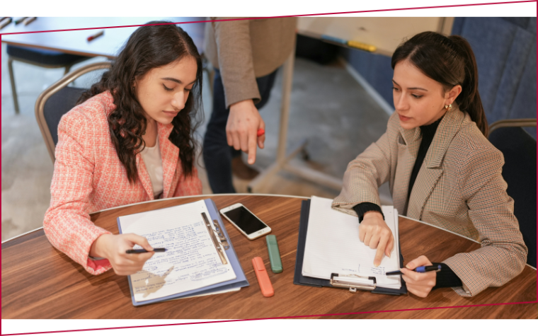 Two women sitting at a table with notebooks and cell phones