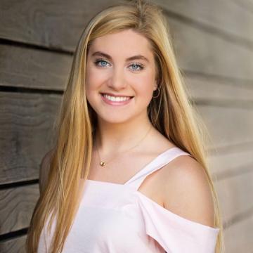 A person smiling in front of a wooden wall.