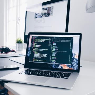 A MacBook with lines of code on its screen on a busy desk