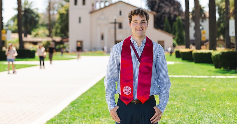 Valedictorian Charles Silver in a button up shirt with commencement scarf on Palm Drive with Mission Church in background image link to article