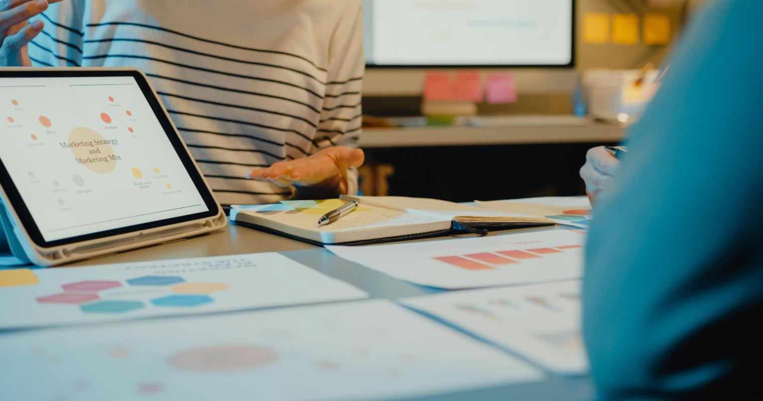 Team of professionals reviewing graphs and data on a tablet during a marketing meeting in modern office image link to article