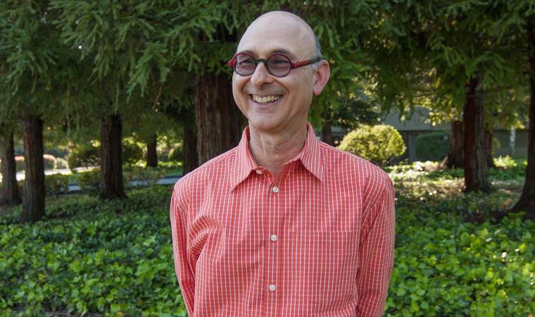 A person wearing glasses and a red striped shirt stands in a green garden.