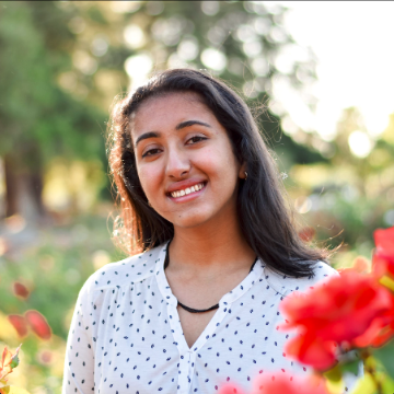 A person smiling in a garden with red flowers.