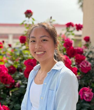 A person smiling in a garden of red flowers.