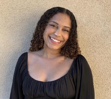 A person smiling in front of a textured wall.