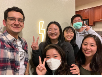 Group of six people smiling and making peace signs indoors.