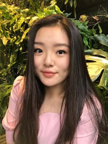 Young woman in a garden, wearing a light pink top.