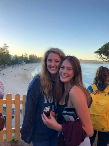 Two people smiling near a beach with a sunset in the background.