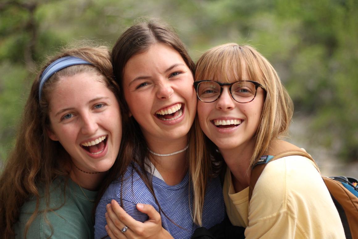 Three smiling people in a close outdoor group.