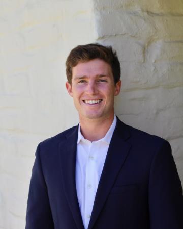 A person smiling in formal attire outdoors.