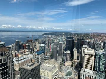 Alt text: Aerial view of Seattle's downtown buildings and waterfront under a blue sky.