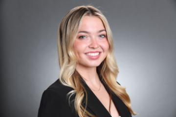 A woman with a smile, dressed in business attire against a gray background.