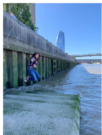 A person standing next to a river with buildings in background.