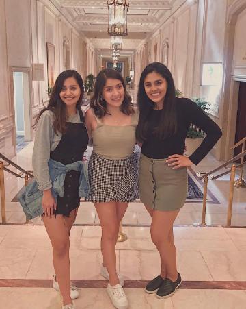 Three women standing and smiling together in a stylish indoor setting.