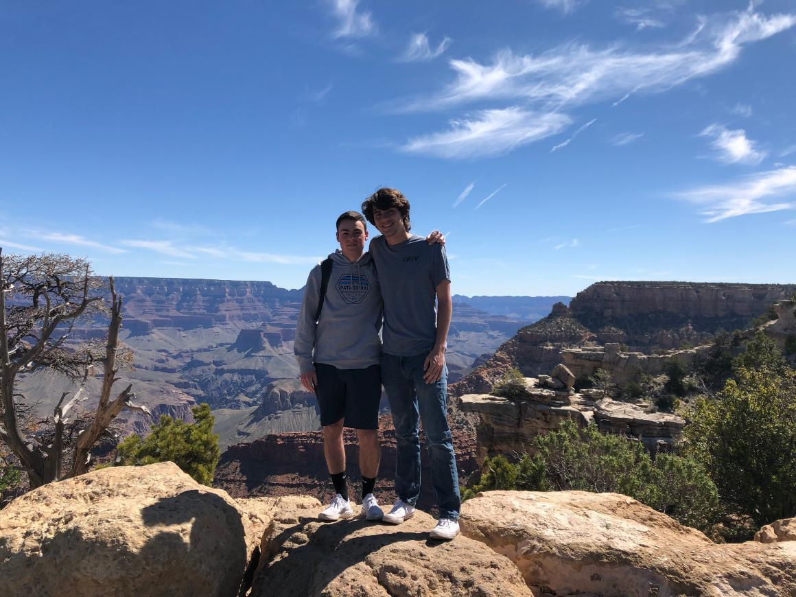 Two people standing on rocky terrain with a scenic canyon view.