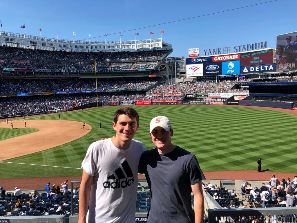 Two people standing in front of a baseball field, smiling at the camera.