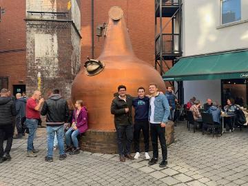 A group of people posing by a large copper brewing vat outdoors.