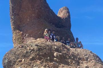 A group of people hiking on a rocky hill against a clear blue sky.