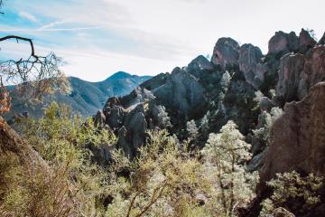 Mountain landscape with trees and jagged peaks under a partly cloudy sky.