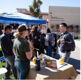 Group of people gathered outdoors near a booth with a display.