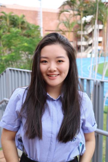 A person smiling outside with trees and buildings in the background.