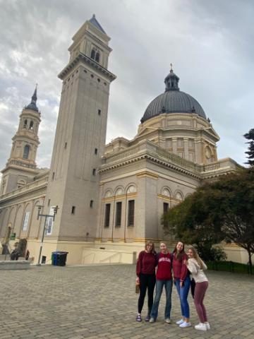 Four people standing outside a large historic building with towers and a dome.