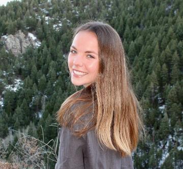 A person smiling with greenery in the background.