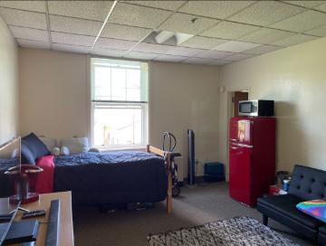 Office space with desk, computer, shelves, and couch near a window.