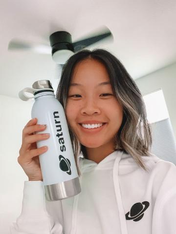 Person wearing white hoodie holding a silver water bottle, smiling.