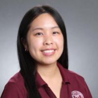 A woman wearing a maroon polo shirt with a university logo.