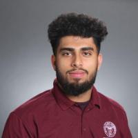 A person in a maroon shirt with a neutral background.