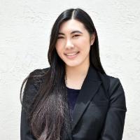 A person in a black blazer, smiling against a white background.