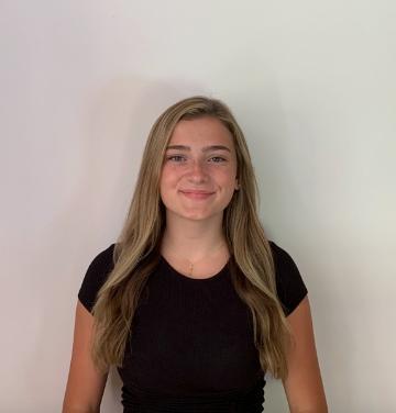 A person in a black shirt standing against a white wall.