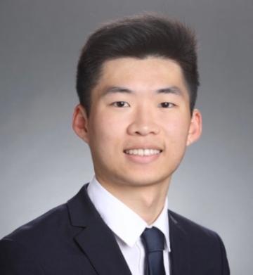 A person wearing a suit and tie against a grey background.