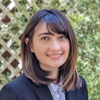 A person smiling in front of a lattice with greenery.