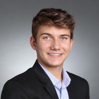 A person wearing a suit against a grey background.