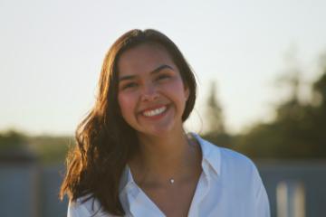 A person smiling outdoors with trees in the background.