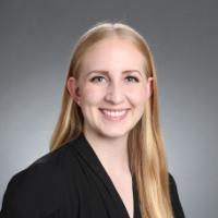 A person smiling in a professional headshot against a gray background.