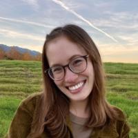 A person in glasses smiling in an open grassy field.
