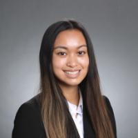 A person wearing a black blazer and white shirt smiling.