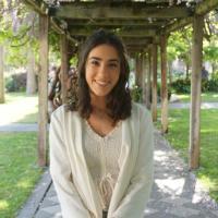 A woman in white smiles under a vine-covered pergola.