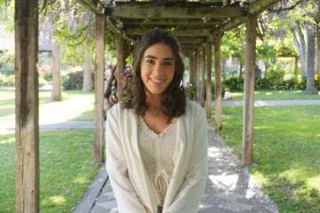 A woman in white smiles under a vine-covered pergola.