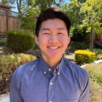 A person in a blue shirt standing outside with greenery in the background.