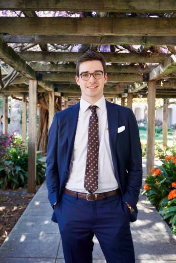 A person in a suit standing in a garden setting.