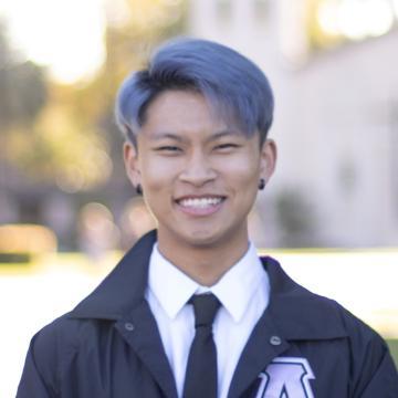 A person smiling outdoors in formal attire.