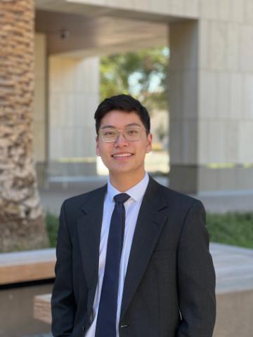 A person in a suit stands outdoors smiling.