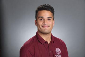 A person in a maroon shirt with a logo stands smiling.